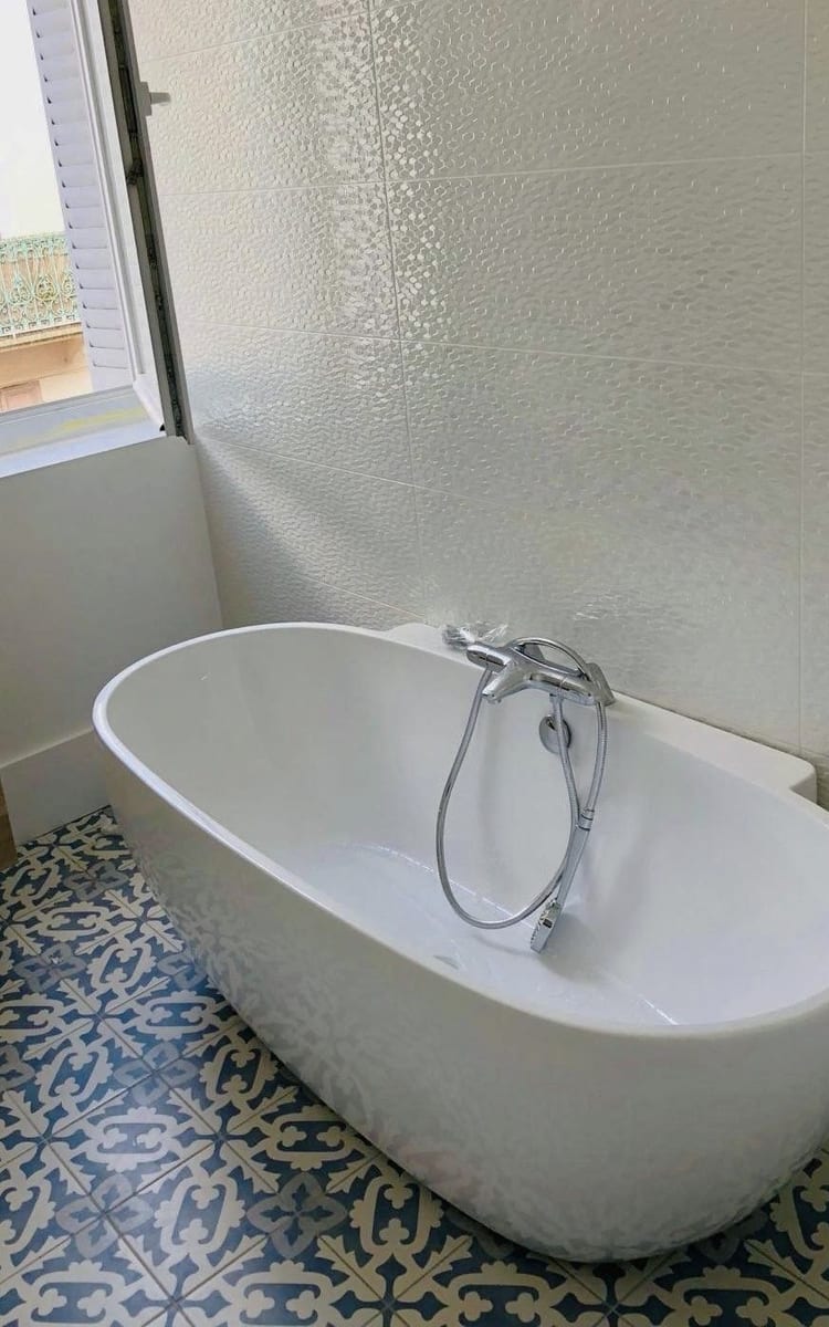 Baignoire îlot posée sur carreaux de ciment dans une salle de bains rénovée