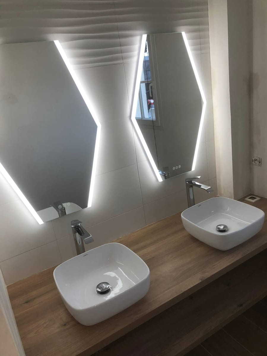 Double vasque sur plan bois et miroirs lumineux dans une salle de bains rénovée